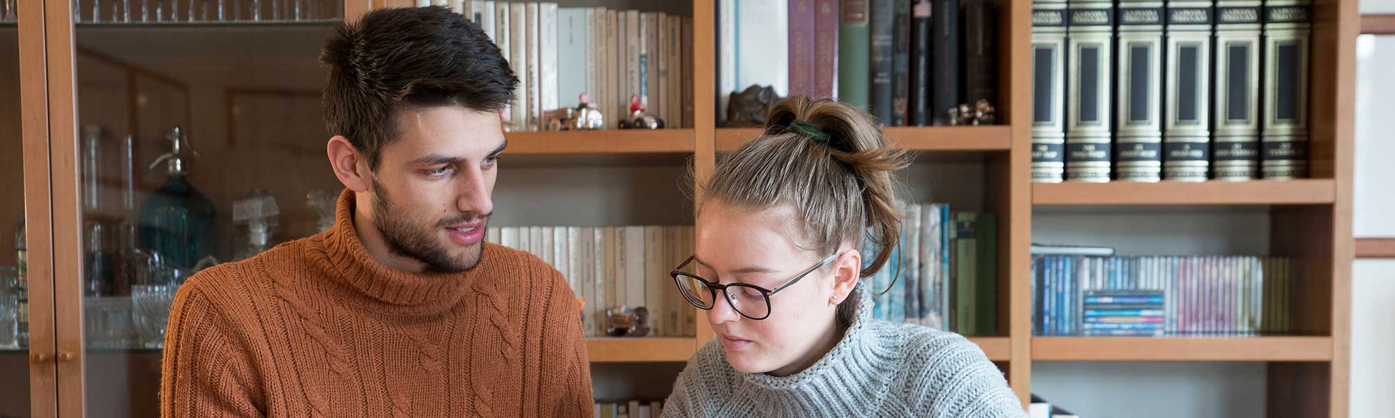 Two students with a bookcase behind them