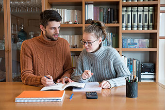 Two students with a bookcase behind them